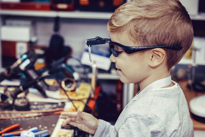 Small boy with magnifying eyeglasses in engineering workshop.  