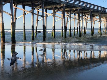 Reflection of wooden pier on sea against sky