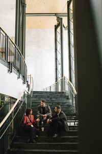 Full length of male and female professionals discussing while sitting on staircase during networking event at convention