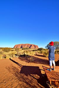 Rear view of woman standing on land against blue sky