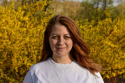 Portrait of young woman standing amidst yellow flowering plants on field