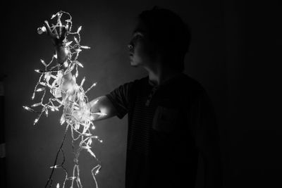 Young man holding illuminated christmas lights while standing in darkroom