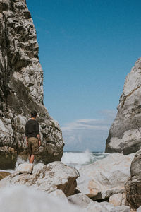 Rear view of man standing on rock formation by sea against sky