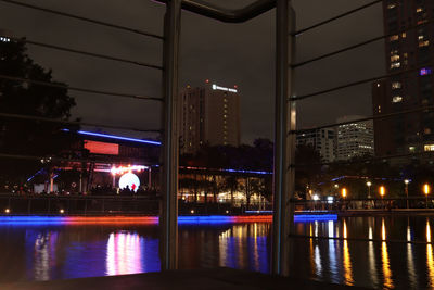 Illuminated buildings by river in city at night