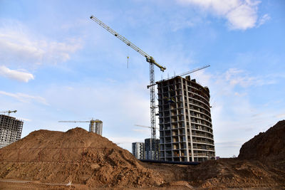 Low angle view of cranes at construction site against sky