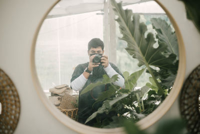 Reflection of man photographing through smart phone on window