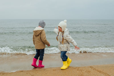 Two little girls in rubber boots stand on the seashore in autumn, spring. sisters play 