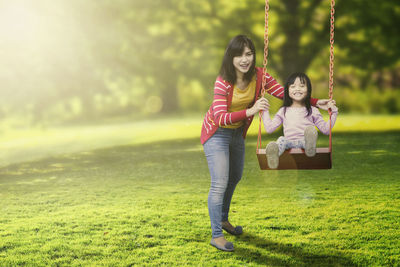 Mother pushing daughter on swing in park