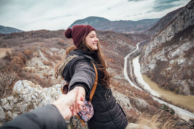 Cropped image of person holding woman hand standing on mountain against sky