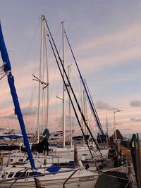 Sailboats moored at harbor against sky during sunset