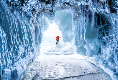 Person standing on snow seen through cave entrance