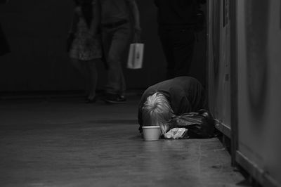 Beggar leaning on floor while people walking in background