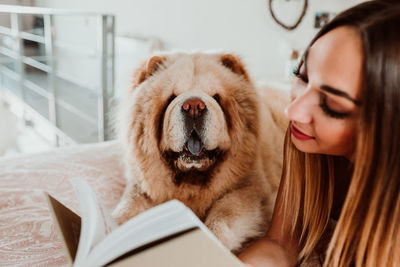 Young woman reading book while lying with dog on bed