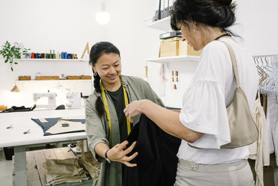 Smiling sales staff assisting female customer trying trousers at workshop