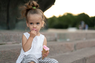 Cute girl eating ice cream sitting outdoors