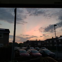 Cars on road by buildings against sky during sunset