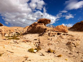 Distant view of man standing on rock formation against cloudy sky