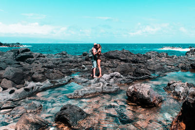 Woman standing on rock at sea shore against sky