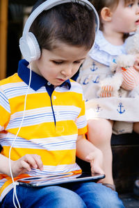 Cute boy listening music with sister outdoors