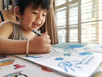 Close-up of smiling boy drawing on book