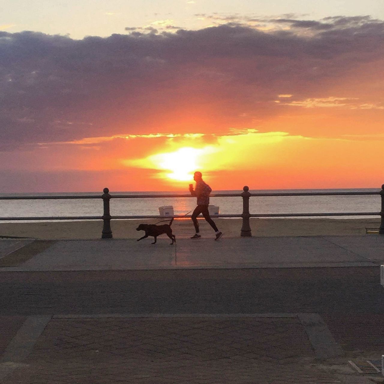 SILHOUETTE PEOPLE RIDING ON BEACH AGAINST ORANGE SKY