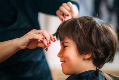 Hairdresser's hands with scissors cutting boys hair in hair salon