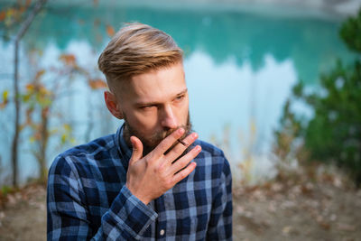 The bearded man smokes. handsome stylish man in plaid shirt with cigarette.