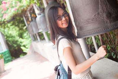 Portrait of young woman striking bell while standing outdoors