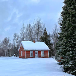 White house on snow covered field by trees against sky