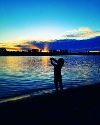 Silhouette man standing by lake against sky during sunset