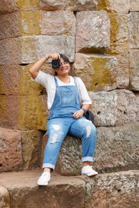 Full length of girl photographing against stone wall