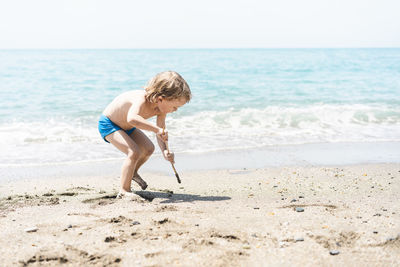 Cute little boy playing with sand at the beach on summer vacation.