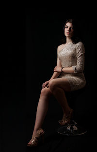 Portrait of young woman sitting against black background