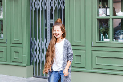 Happy girl looking away while standing against shop in city