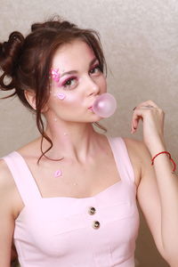 Young woman with pink make-up chewing gum against wall