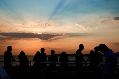 Silhouette people by sea against sky during sunset