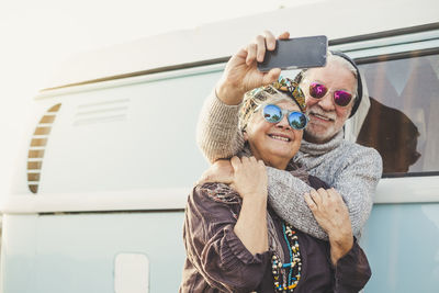 Couple taking selfie with mobile phone while standing against motor home