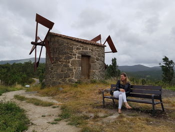 Full length of woman sitting on bench against sky