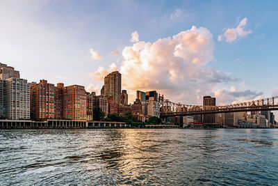 Bridge over river by buildings against sky in city