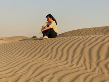 Man on sand dune in desert against clear sky