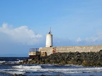 Lighthouse on beach by sea against sky