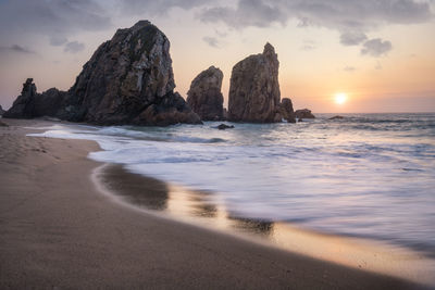 Rock formation on beach against sky during sunset