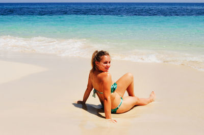 Smiling blonde woman sitting on tropical beach