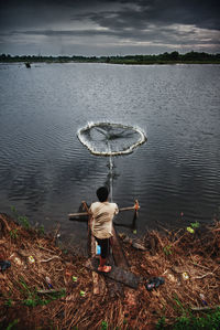 Rear view of man fishing at lake during sunset