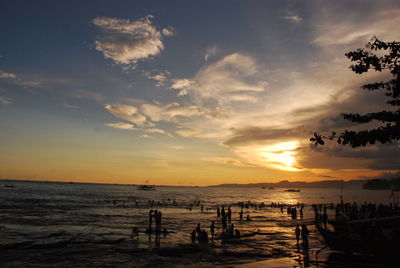 Silhouette people in sea against sky during sunset