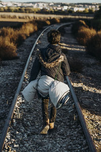 Kid hiking in the woods caring a sleeping bag walking in a train track