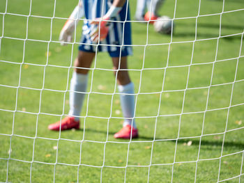 Young football goalkeeper in playground. out of focus. view through the football gate net.