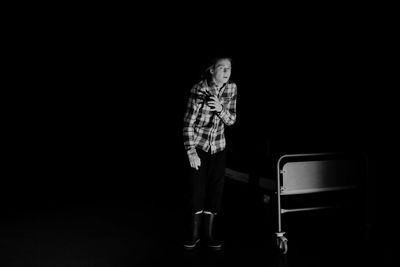 Full length of teenage boy standing by bed against black background