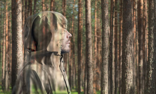 Double exposure of man wearing hood and trees