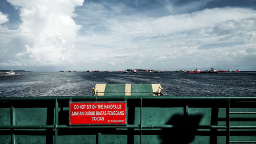 Text on railing by sea against sky